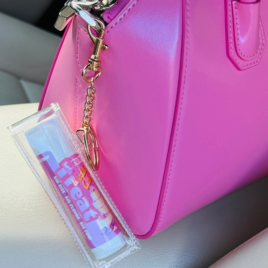 Pink handbag with a keychain and clear case on a light-colored surface