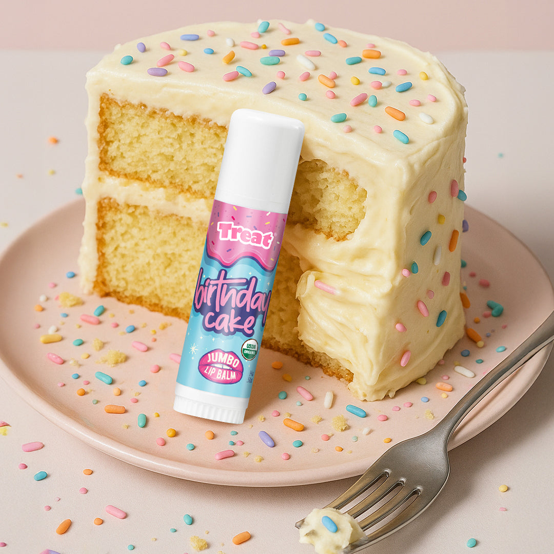 Layered cake with colorful sprinkles on a plate, accompanied by a lip balm labeled 'Treat Factory Birthday Cake'.