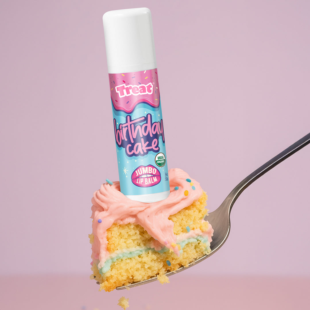 Lip balm labeled 'Birthday Cake' on a slice of cake with pink frosting against a purple background